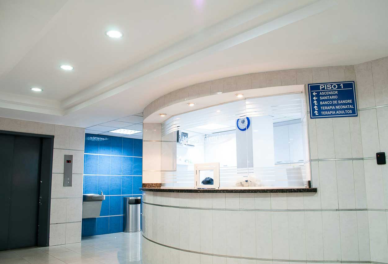 A brightly-lit reception area. The counter is curved and the room is covered in while tiles.