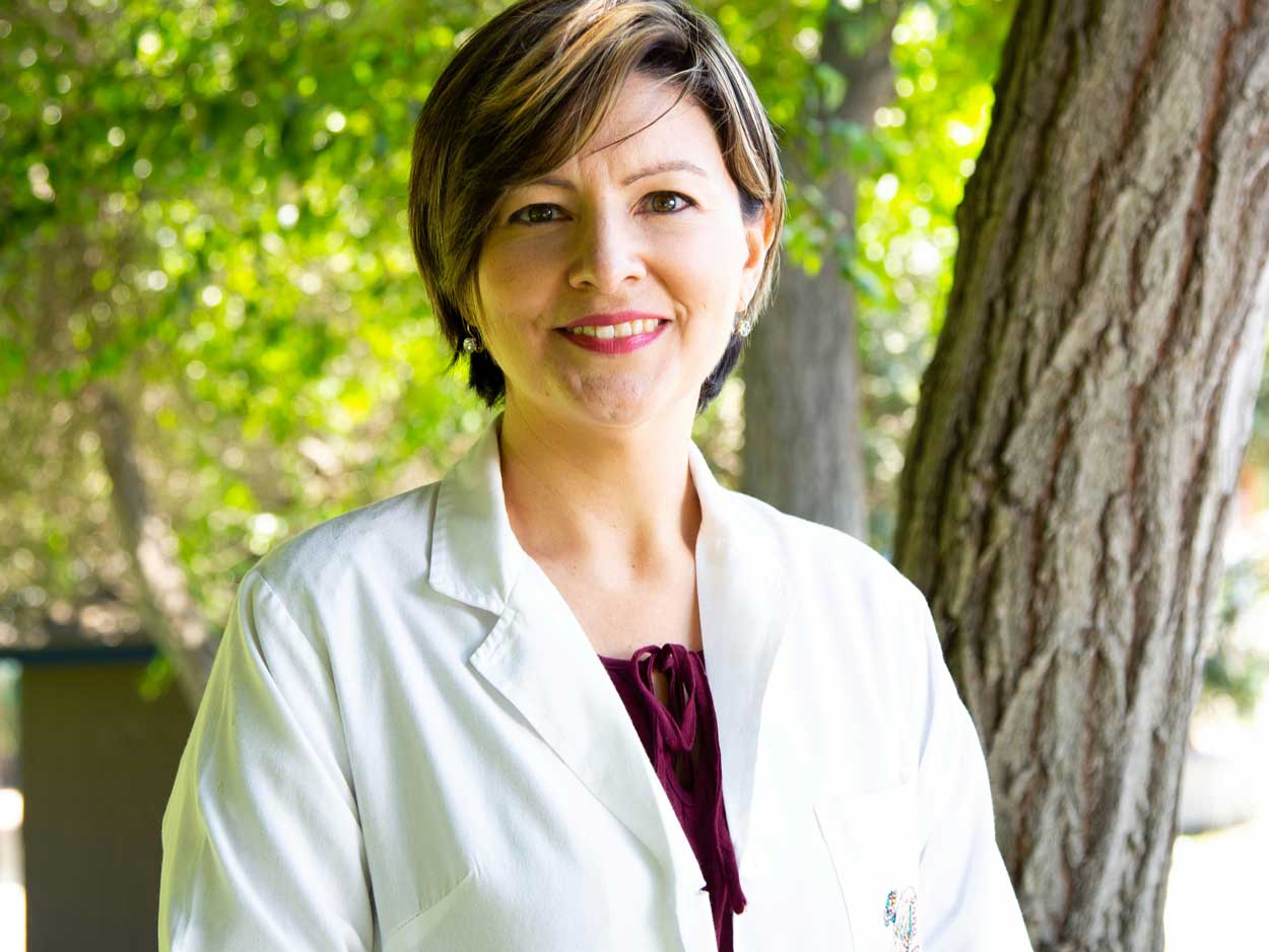 A woman with short, highlighted hair and a white coat smiles for the camera.