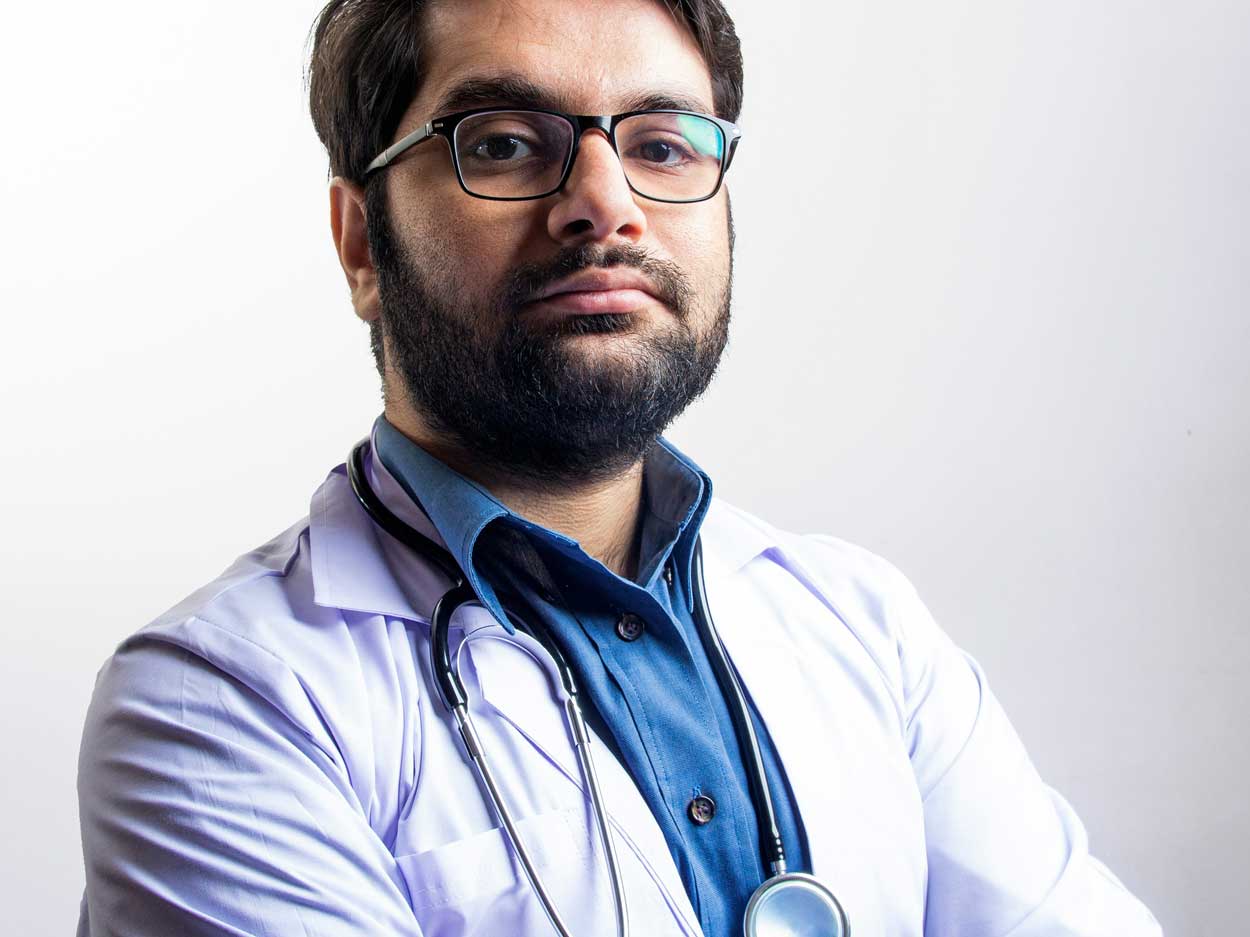 A young man with dark hair, glasses, and a dark beard poses confidently.