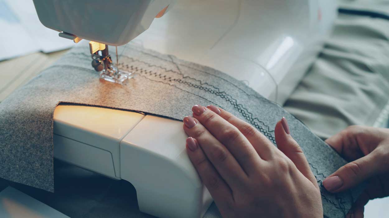 A closeup of hands guiding a strip of fabric through a sewing machine.