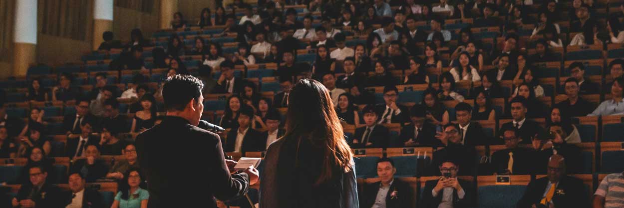Two people give a presentation in front of a large crowd.
