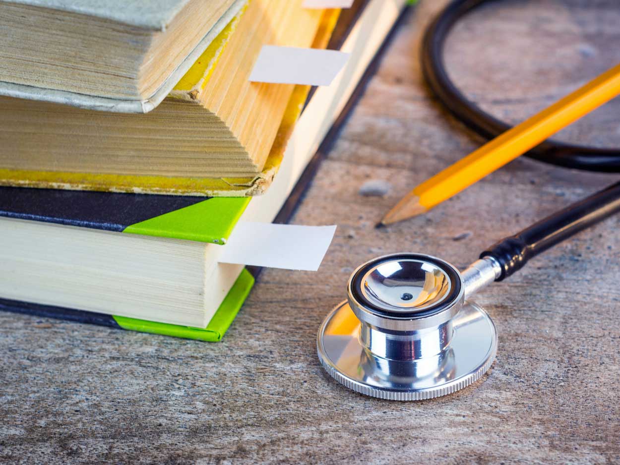 A closeup of a stethoscope sitting next to a pile of tabbed books.